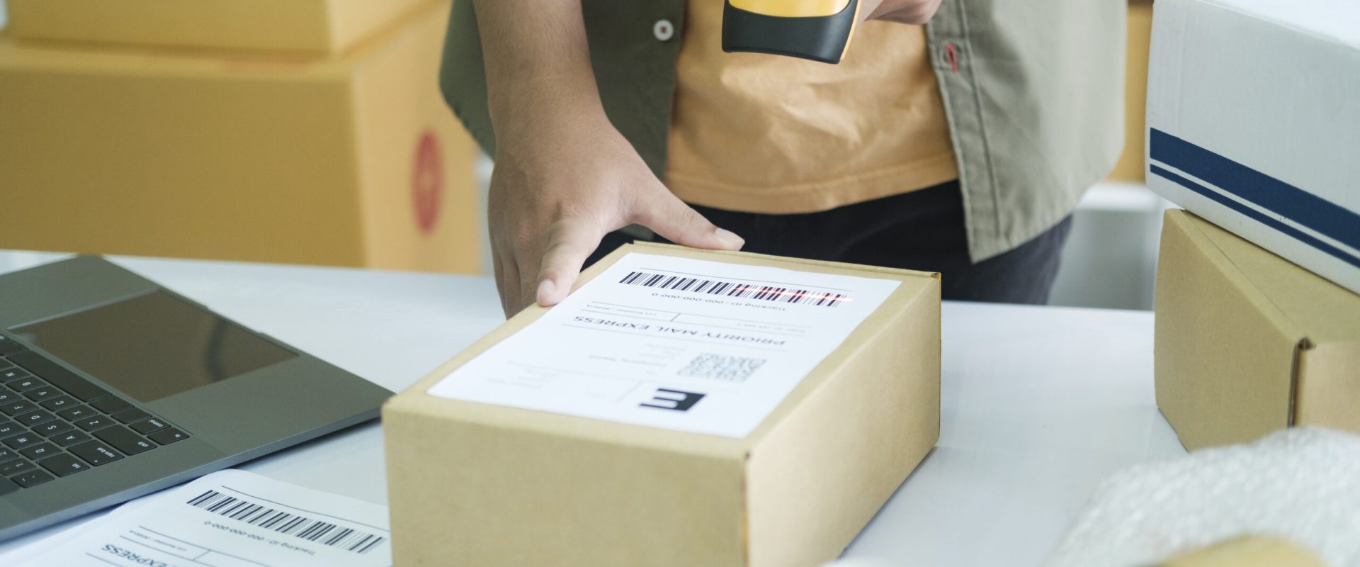 Young male online store seller, owner holding scanner scanning parcel barcode before delivery or shipping to customer. an working at factory warehouse scanning labels on the boxes. E-commerce concept.